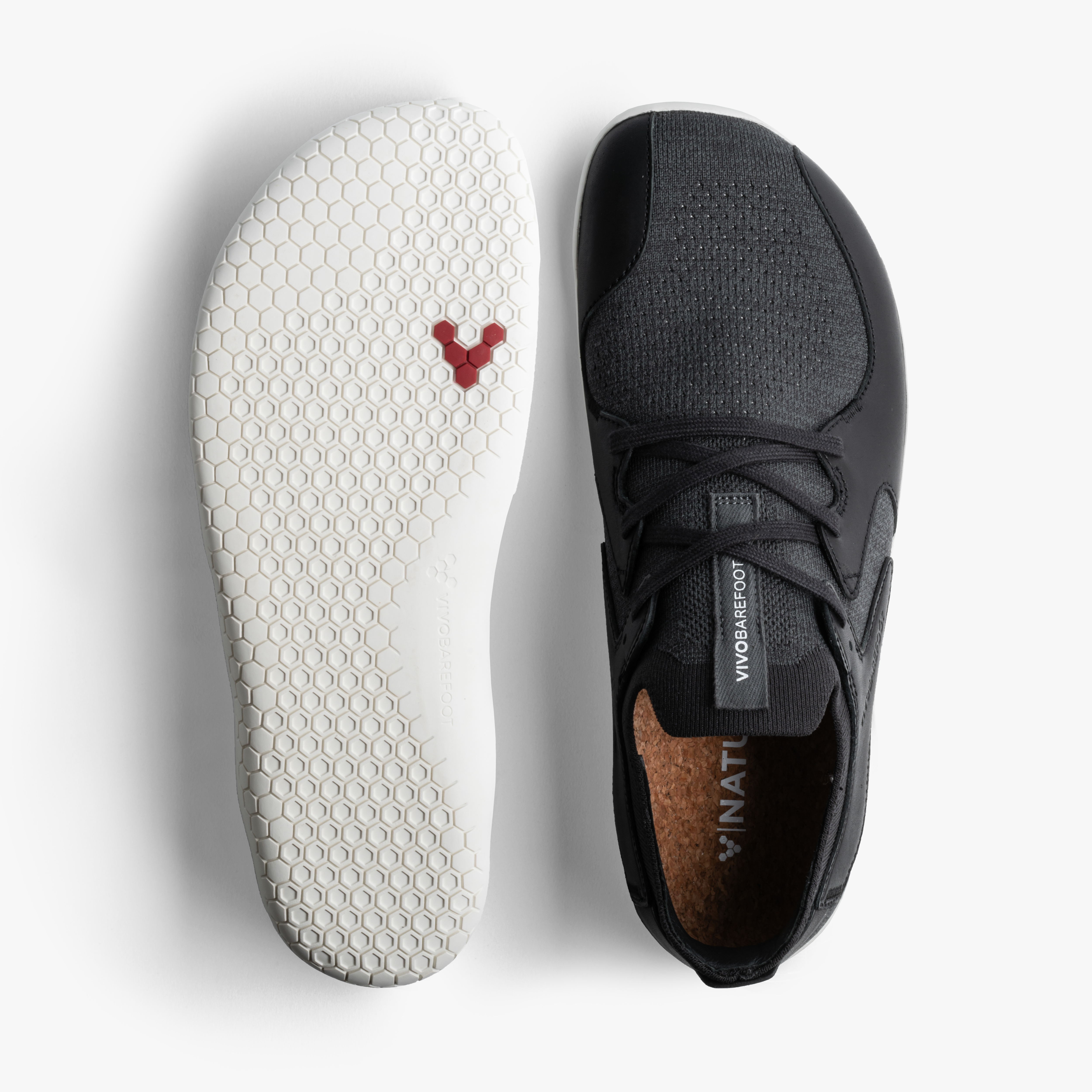 Vivobarefoot Asana III i varianten 'Obsidian', vist ovenfra med én skos hvide, sekskantede sål og den andens sorte tekstiloverdel med kork indersål. Ideel til barfodslivsstil.