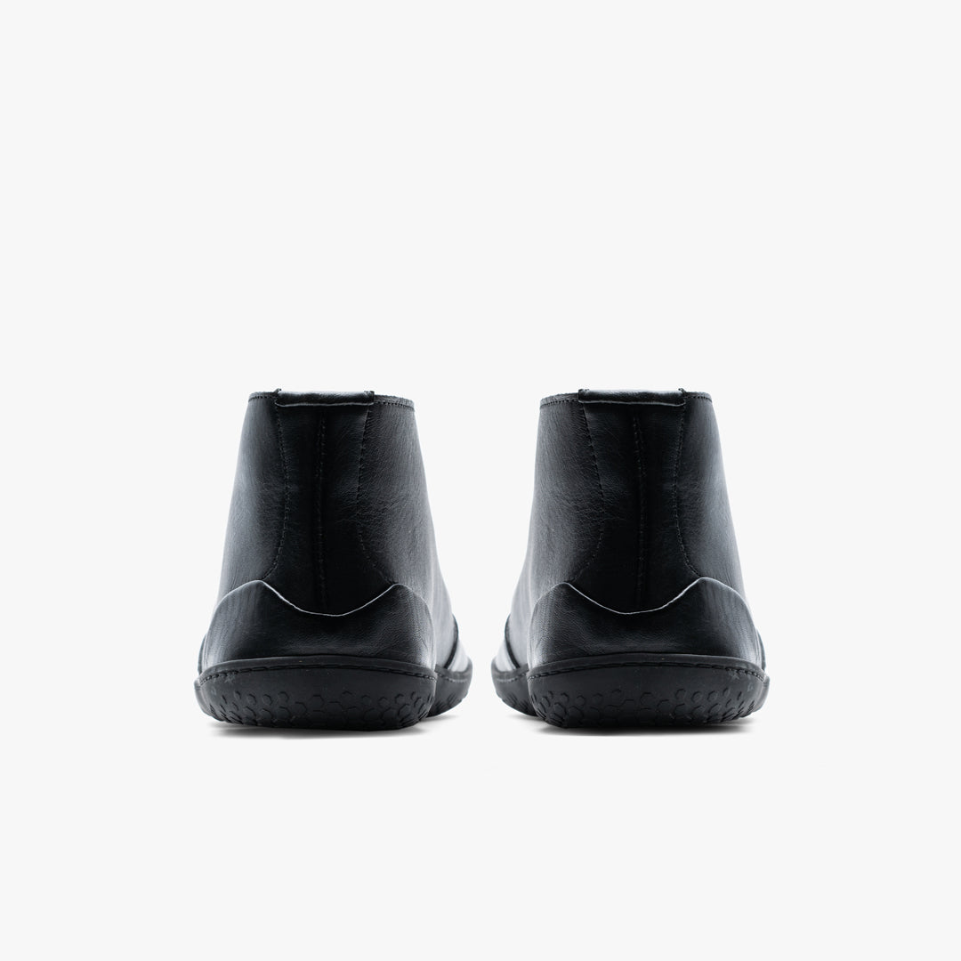 Vivobarefoot Gobi Lux i farven Obsidian, barfodssko til herrer, vist bagfra. Fremstillet af glat sort metalfrit kohudslæder med en minimalistisk sømdetalje og robust sort gummisål.